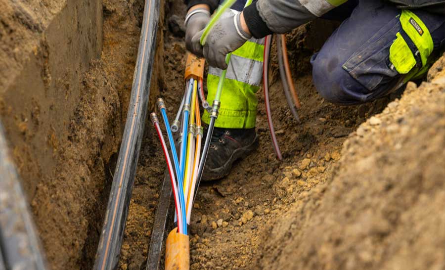 Technician in safety gear organizing colorful fiber optic microducts inside an underground trench during utility installation.