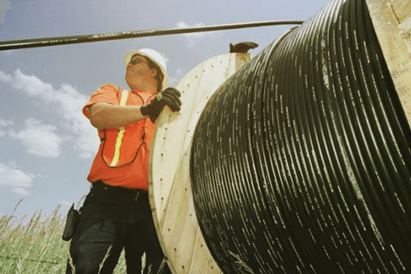 Professional technician working with a large fiber optic cable reel for underground utility installation
